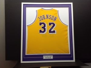 Basketball jersey of Magic Johnson framed with purple mat and engraved plate added at bottom.